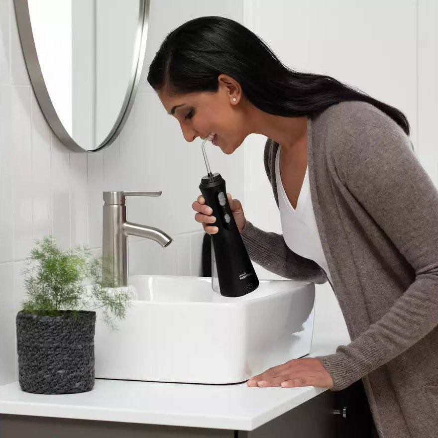 Woman flossing her teeth with a black coloured waterpik water flosser