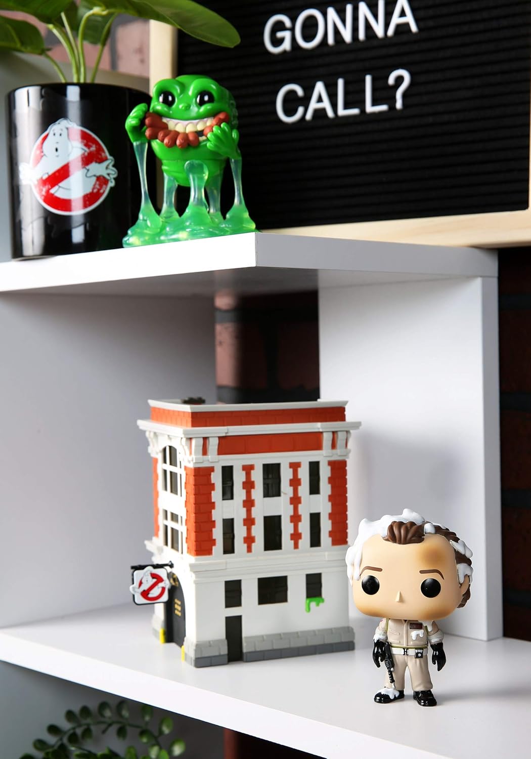 Shelf with Ghostbusters-themed items including a building model, green creature figure, and pop vinyl figure.