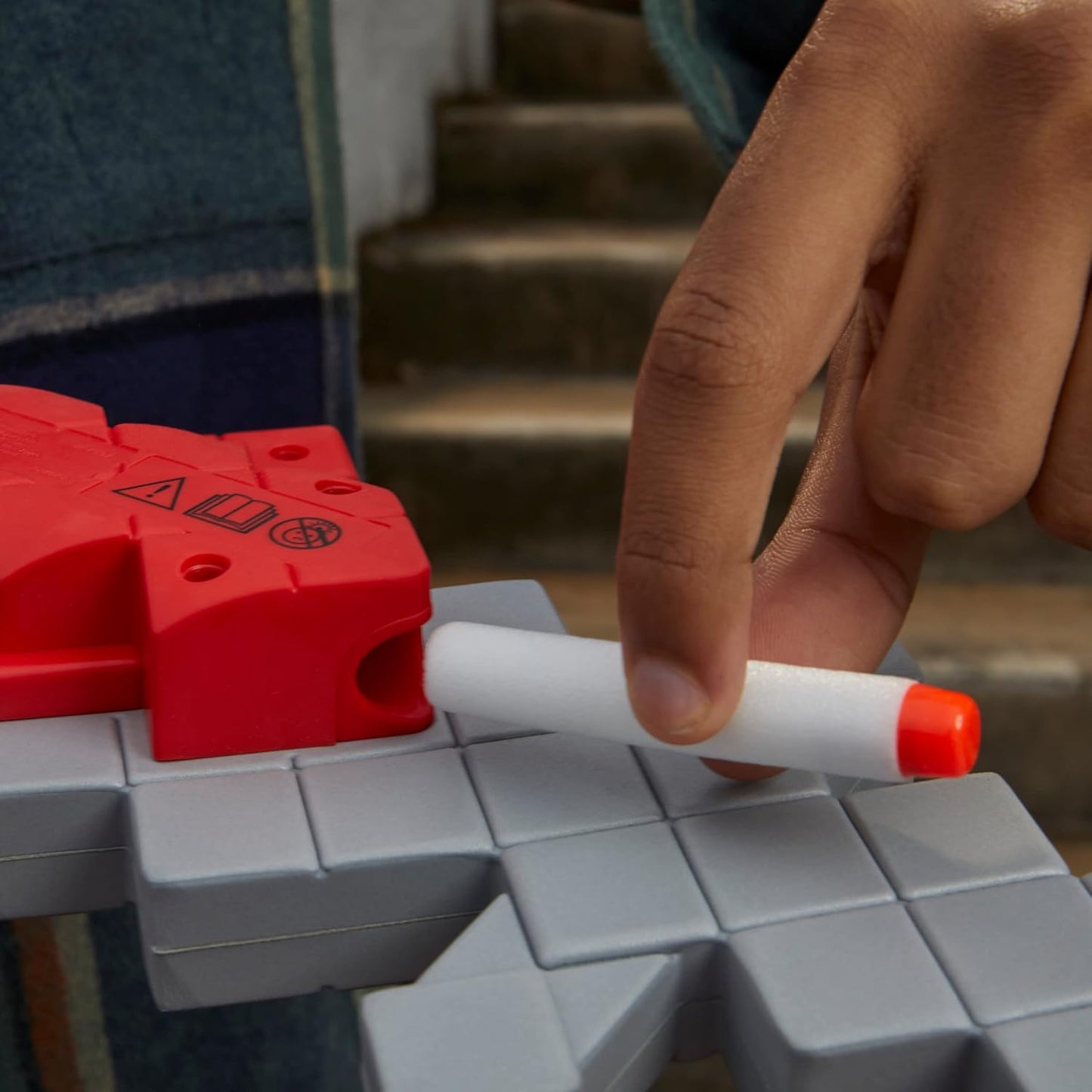 Hand holding a white marker with orange cap over a red and gray toy structure.