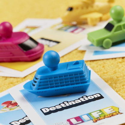 Toy boat on a card with 'Destination LIFE' text, surrounded by other toys on a yellow surface.