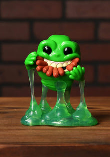 Green monster figurine with a red tongue on a wooden surface with a brick wall background