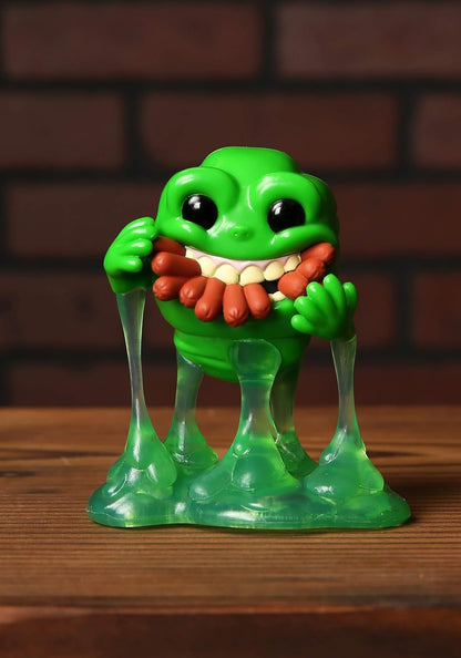 Green monster figurine with a red tongue on a wooden surface with a brick wall background