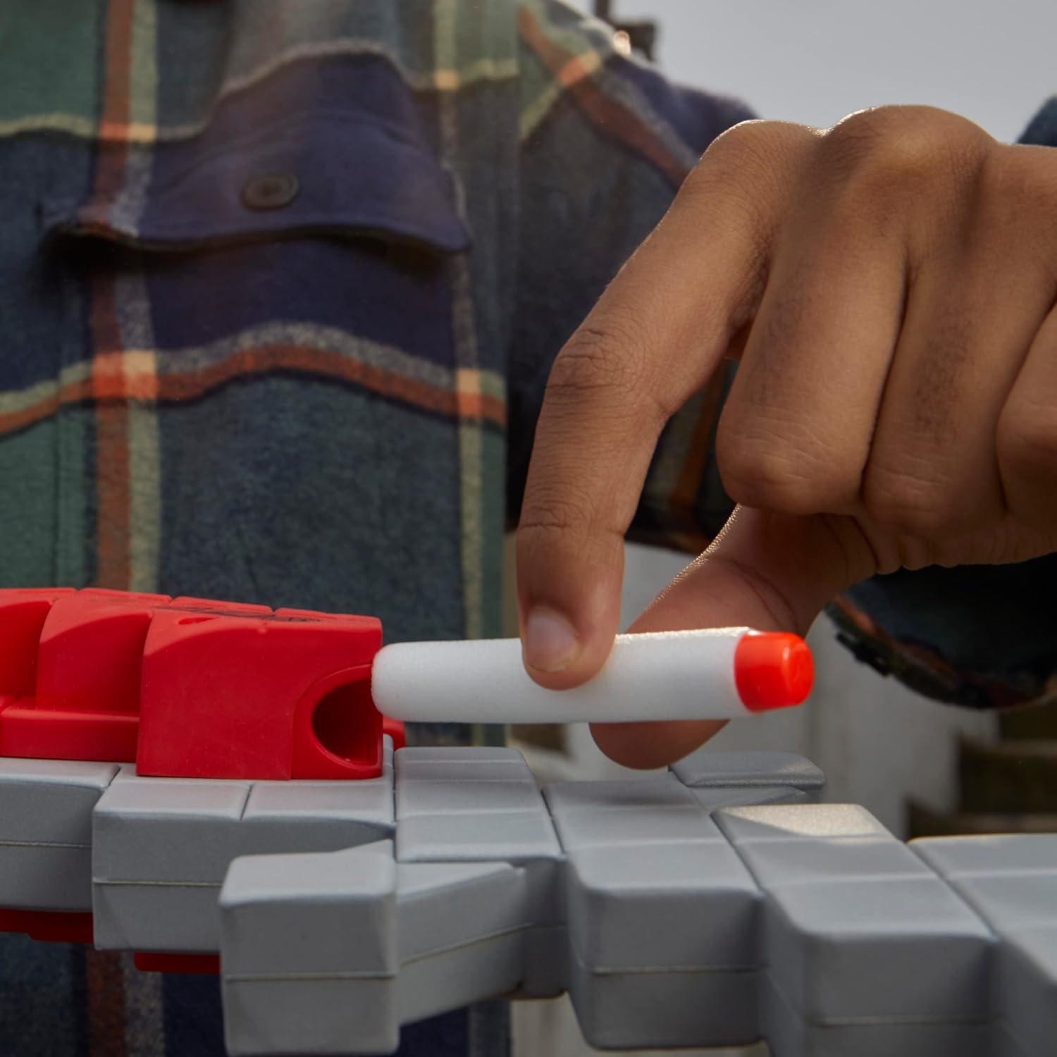 Hand holding a red and white marker over a gray and red toy structure with a plaid shirt in the background.