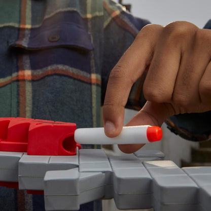 Hand holding a red and white marker over a gray and red toy structure with a plaid shirt in the background.