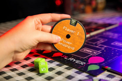 Hand holding a round game component with text on a colorful board game background