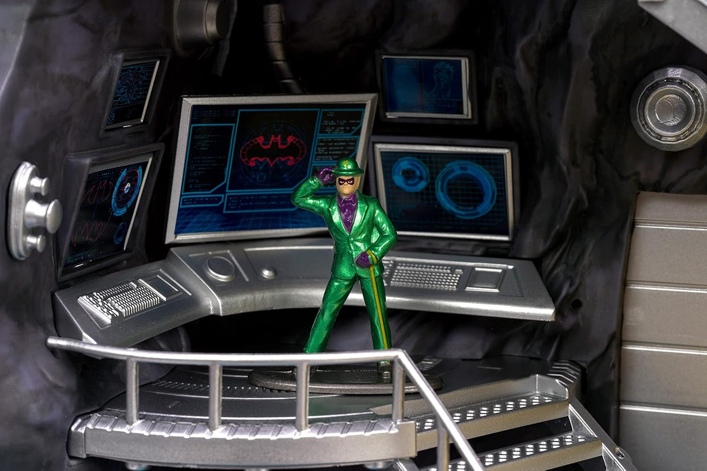 Toy figure in a green suit standing on a control panel with multiple screens displaying futuristic graphics.