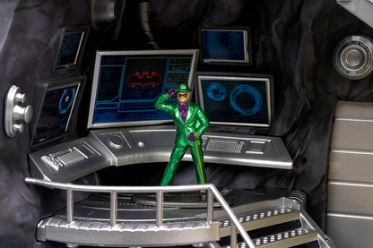 Toy figure in a green suit standing on a control panel with multiple screens displaying futuristic graphics.