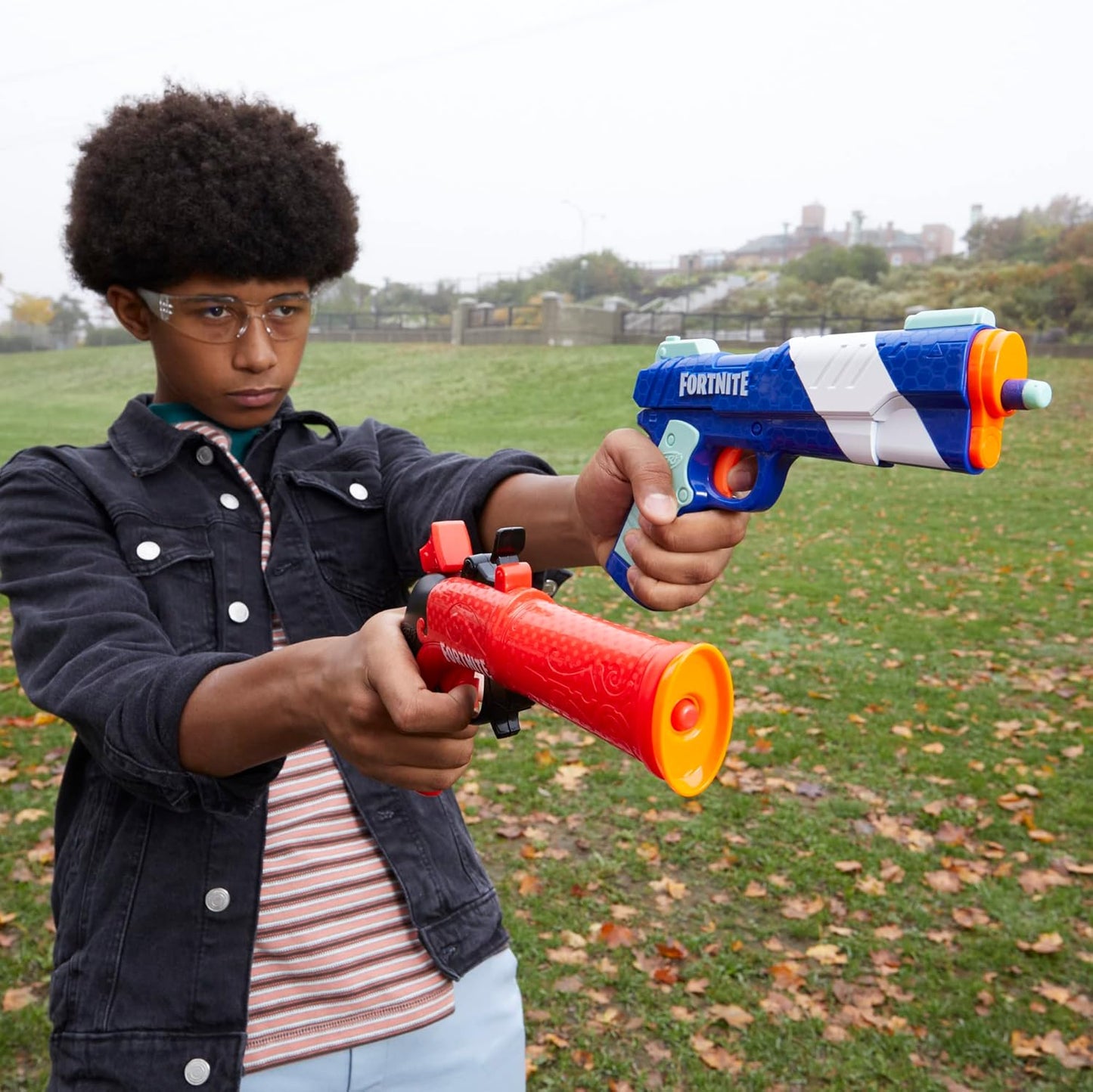 Person holding two toy guns outdoors on a grassy field