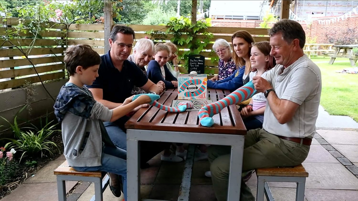 Family and friends gathered around a table outdoors, playing with a sock puppet.