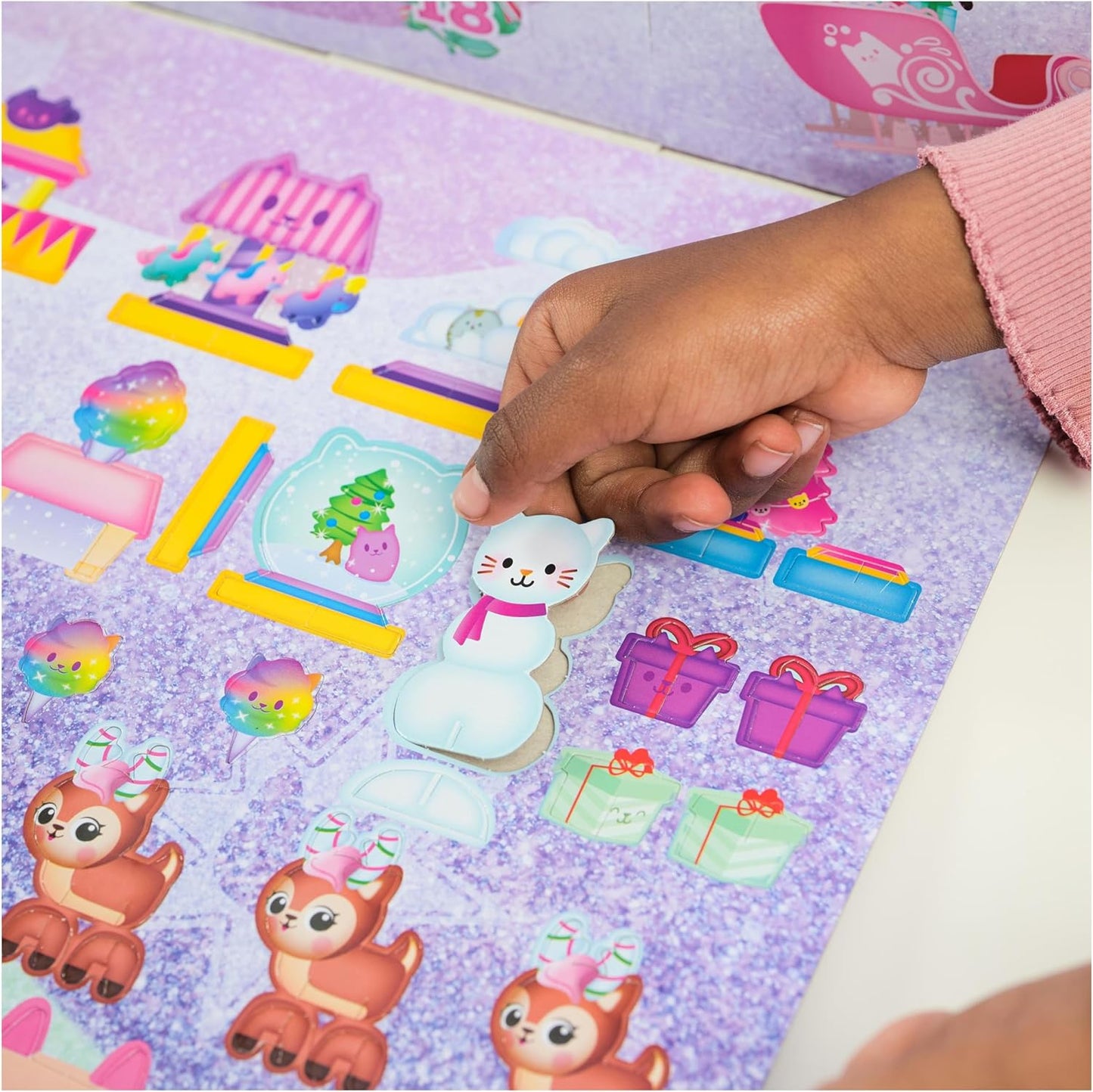 Hand placing a sticker of a cat in a snow globe on a sheet with various stickers.
