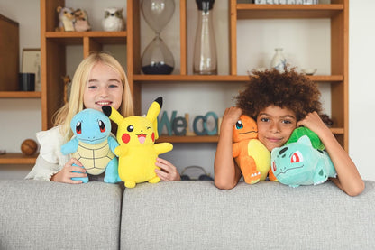 Two children sitting on a sofa holding Pokemon plush toys in front of a wooden shelf.