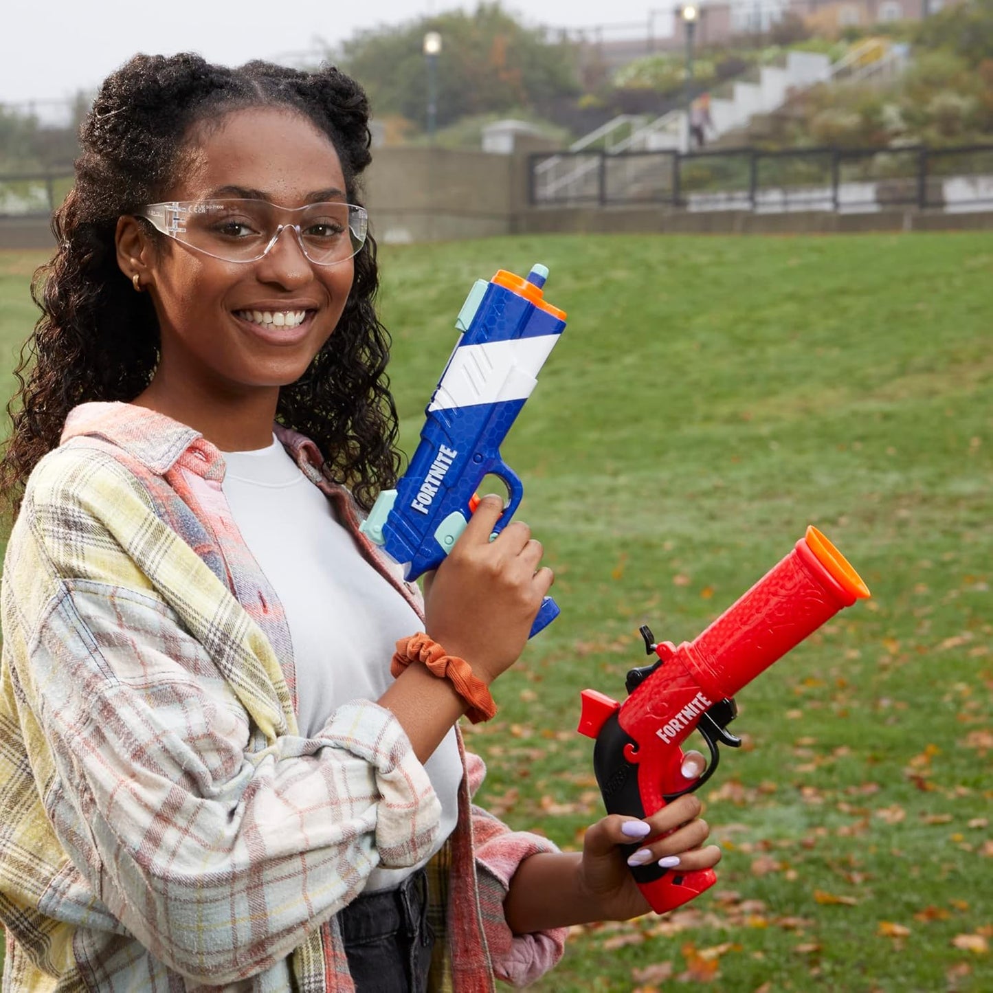 Person holding two water guns in a grassy outdoor area