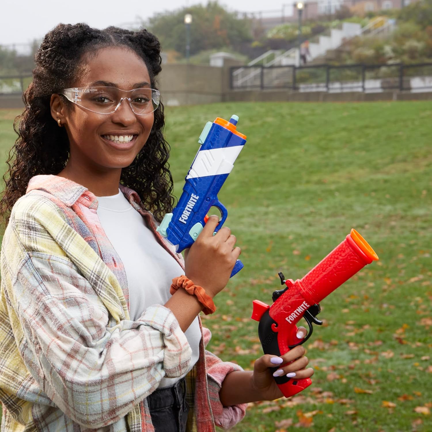 Person holding two water guns in a grassy outdoor area