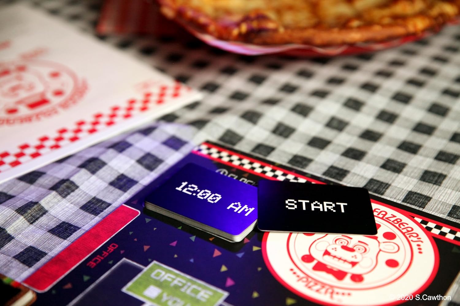 Close-up of a vintage arcade game control panel with '12:00 AM' and 'START' buttons on a checkered tablecloth.