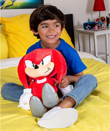 Child holding a Knuckles plush toy on a bed with yellow bedding