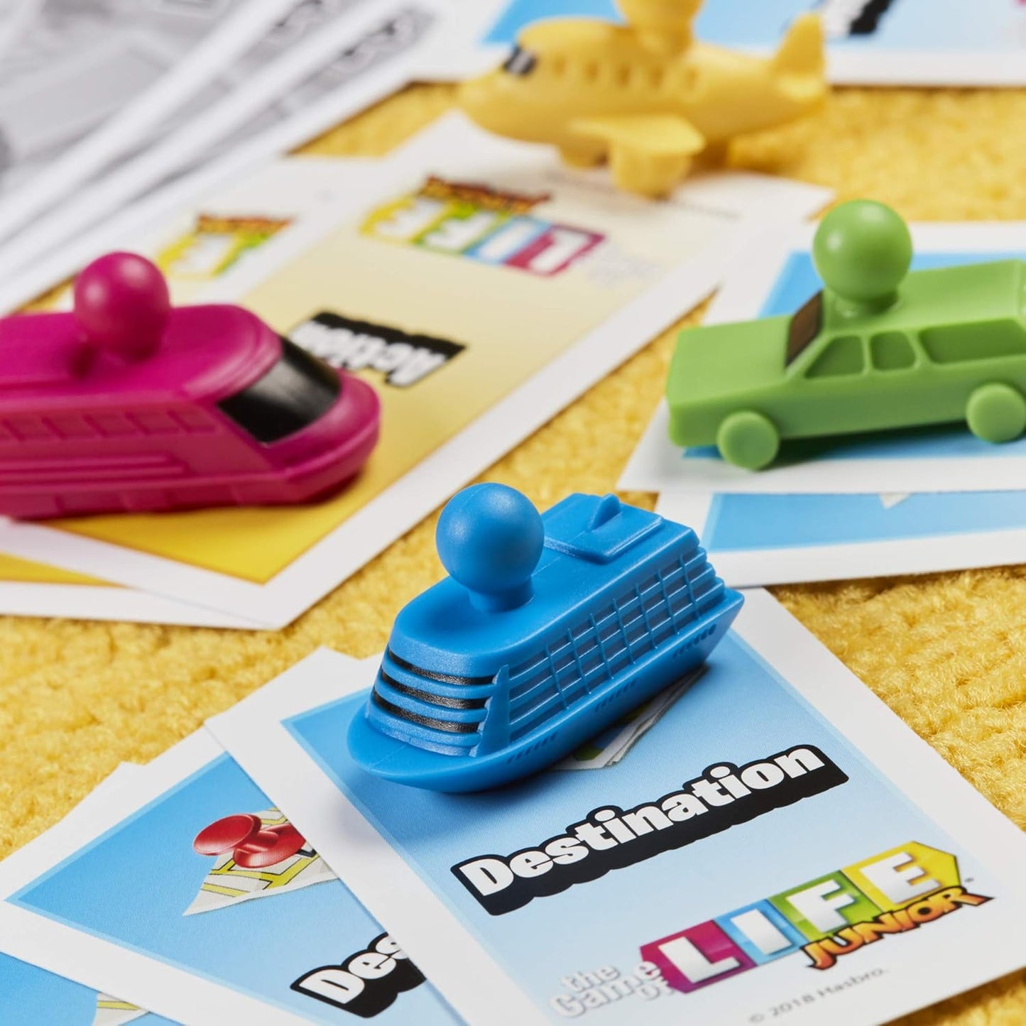 Board game pieces including a blue car, pink airplane, and green truck on game cards.