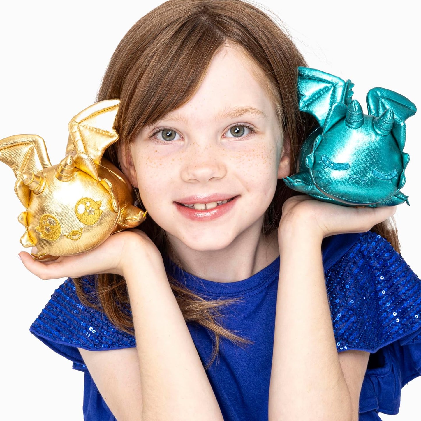 Young girl holding a gold and a turquoise dragon-shaped object against a white background