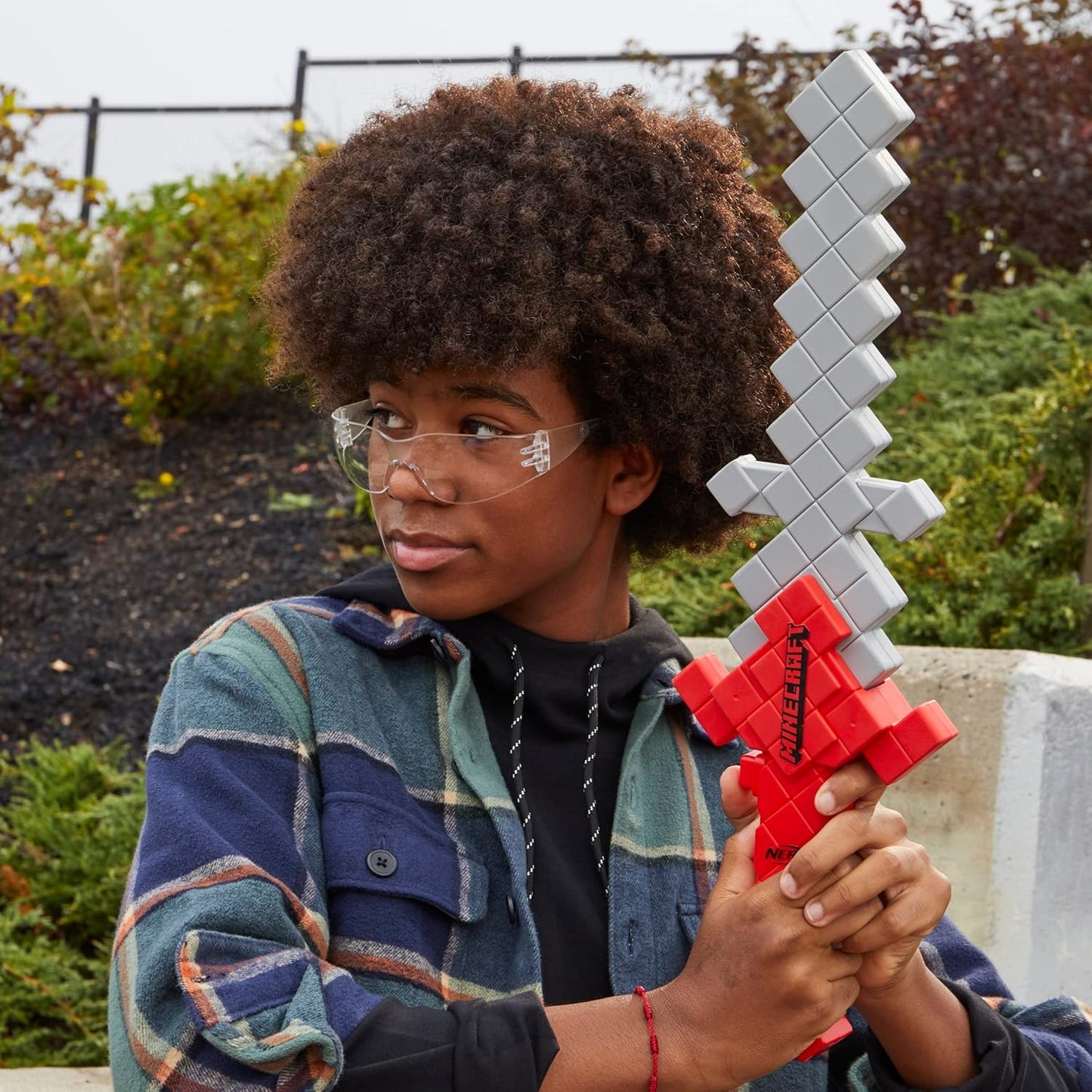 Person holding a pixelated sword outdoors with greenery in the background