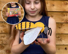 Girl holding a paper wasp model with inset showing a book titled 'Wasp'.