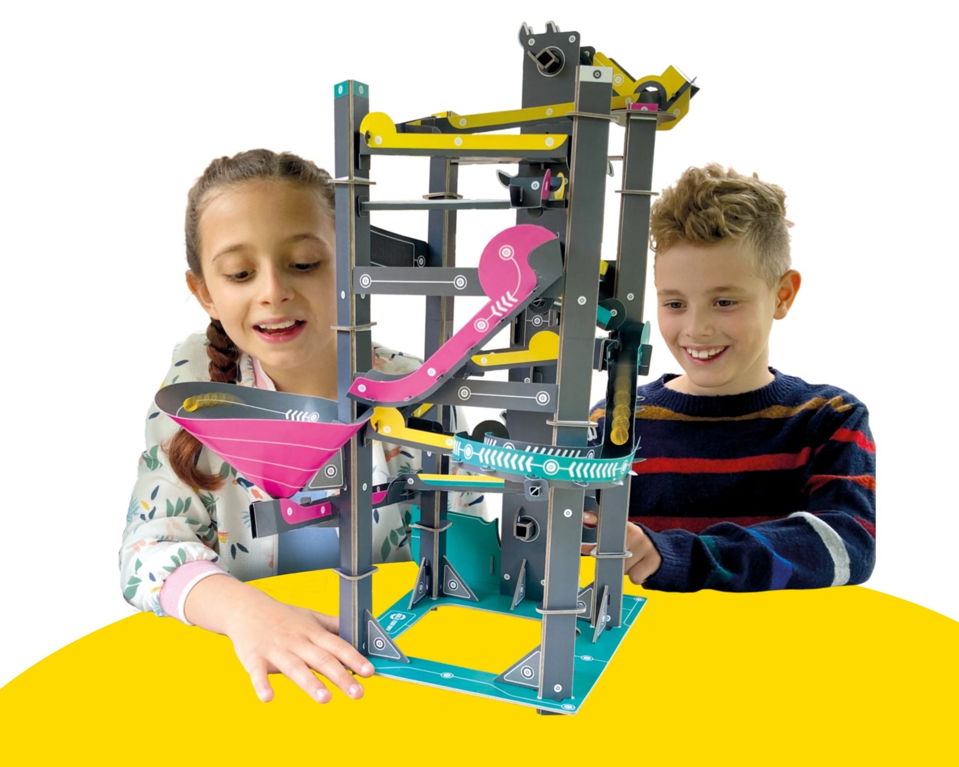 Two children playing with a marble run toy set on a yellow surface.