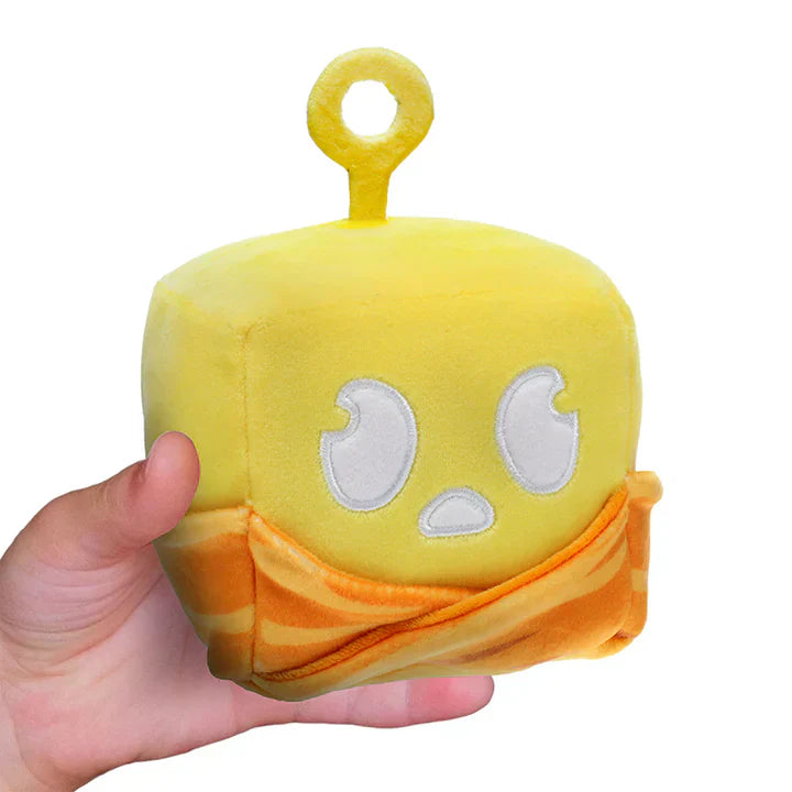 Yellow plush toy with a face and orange shirt held in a hand on a white background
