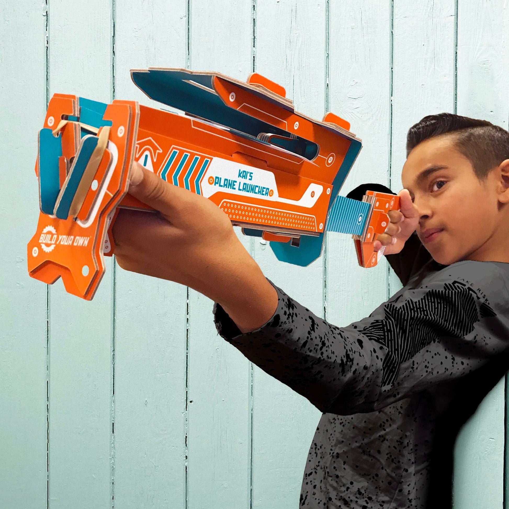 Child holding a plane launcher against a light blue wooden background