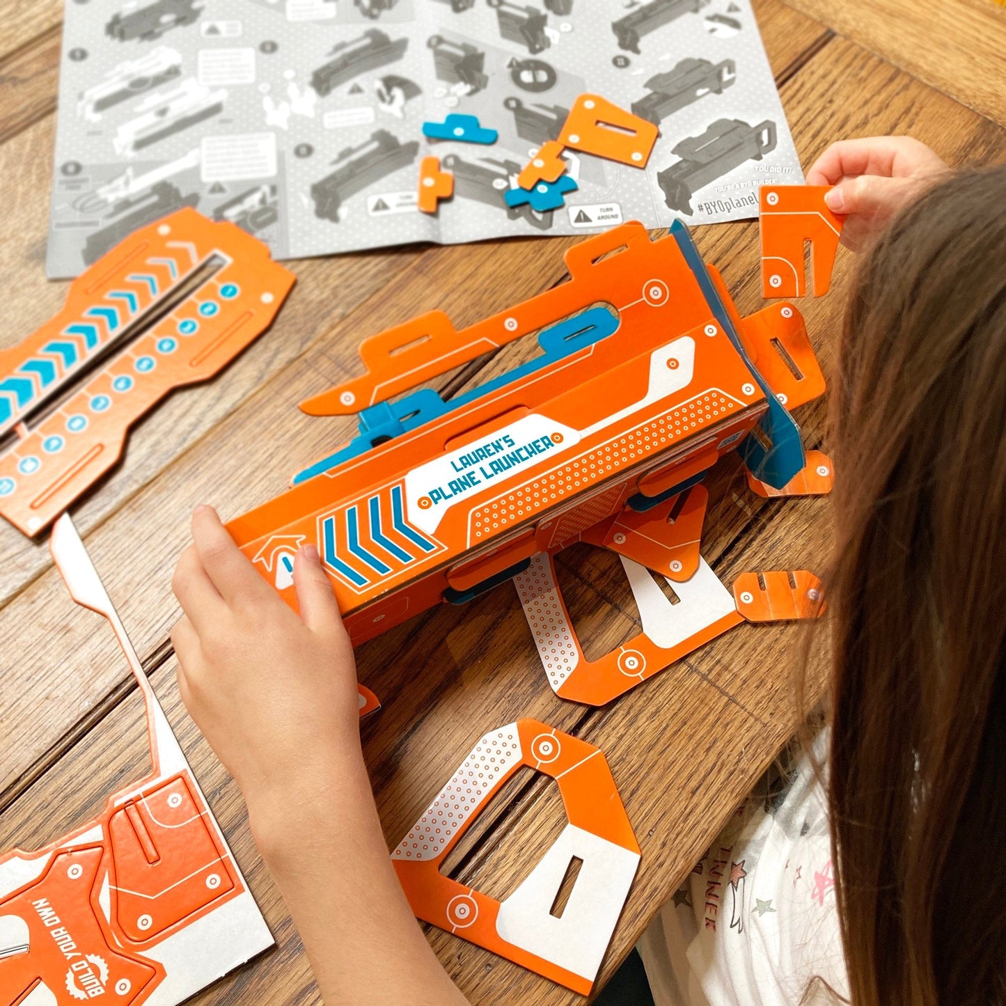 Child playing with an orange and blue toy plane launcher on a wooden table.