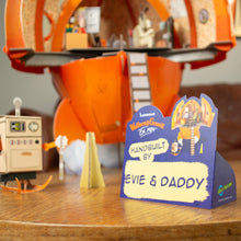 Toy set with a sign indicating 'Handbuilt by Evie & Daddy' on a wooden surface.