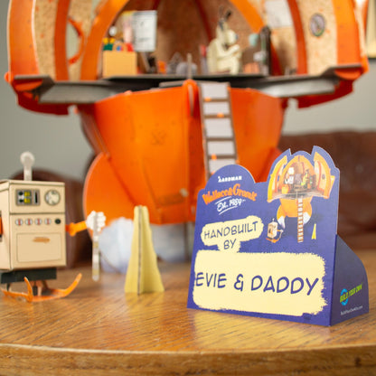Toy set with a sign indicating 'Handbuilt by Evie & Daddy' on a wooden surface.
