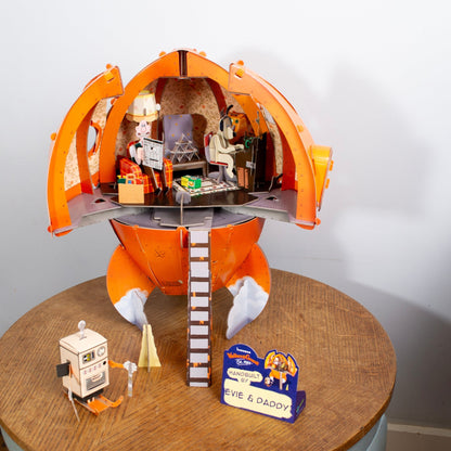 Toy set with an orange rocket, figures, and a sign on a wooden table.