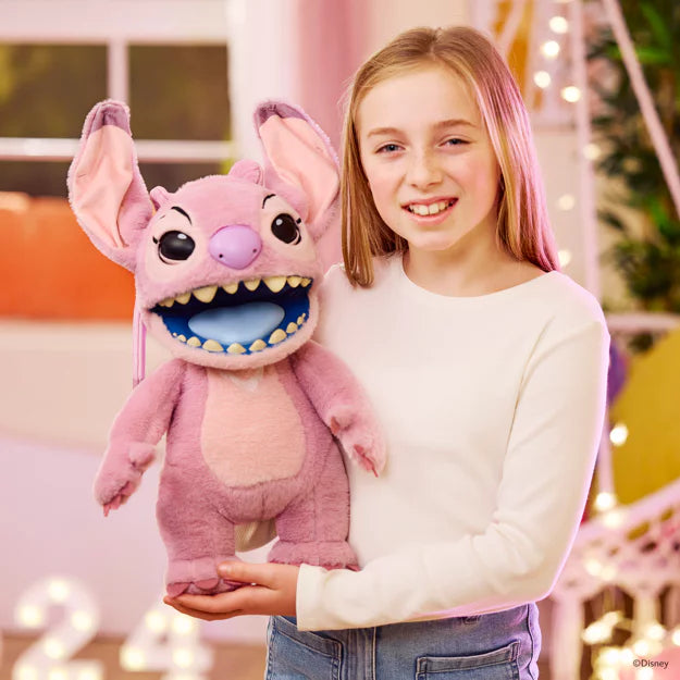 Girl holding a pink plush toy with a large mouth and smiling, in a festive indoor setting.