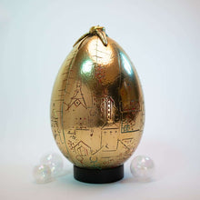 Gold egg-shaped object with engraved patterns on a white background