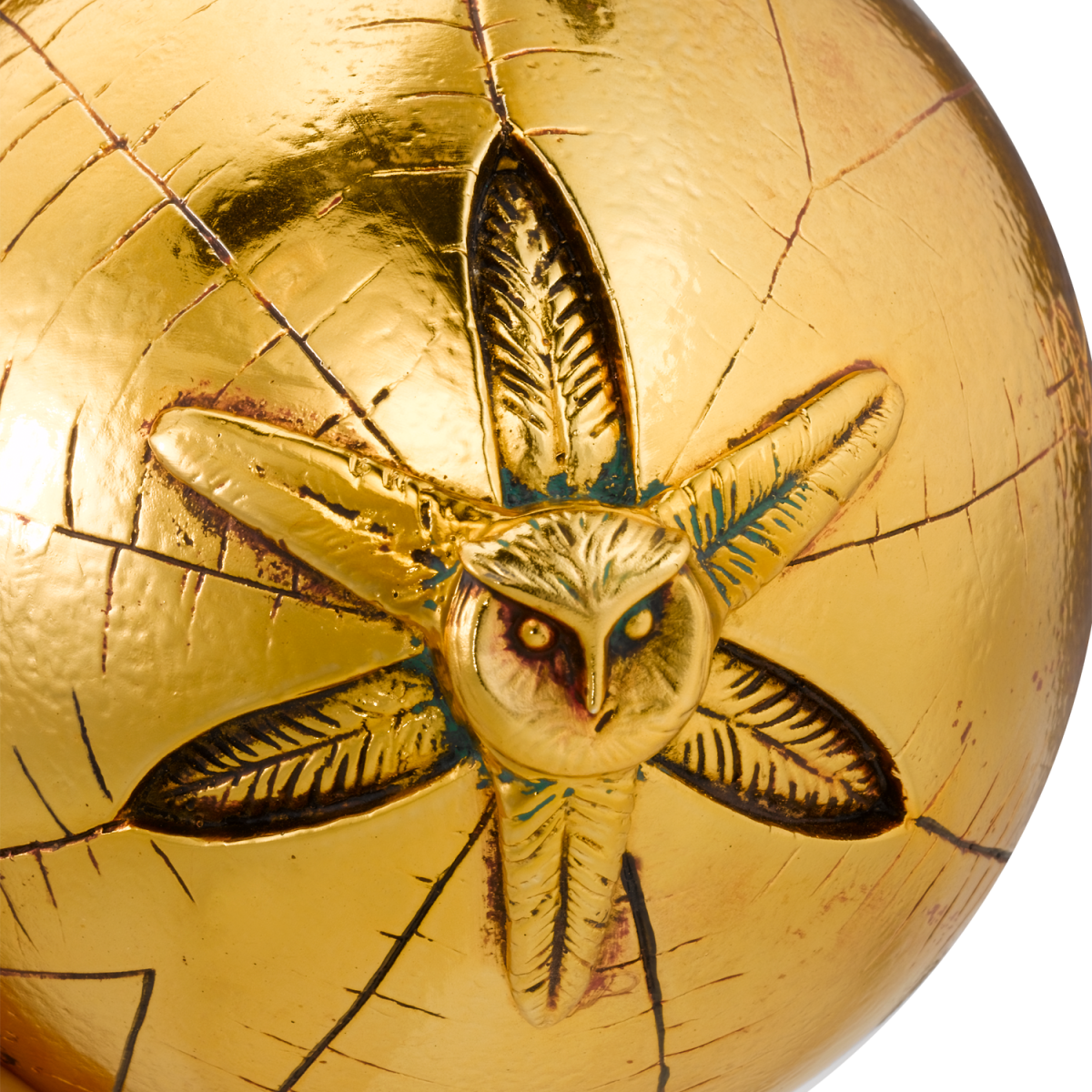 Gold sphere with an embossed design of an owl and feathers on a white background