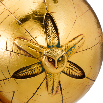Gold sphere with an embossed design of an owl and feathers on a white background