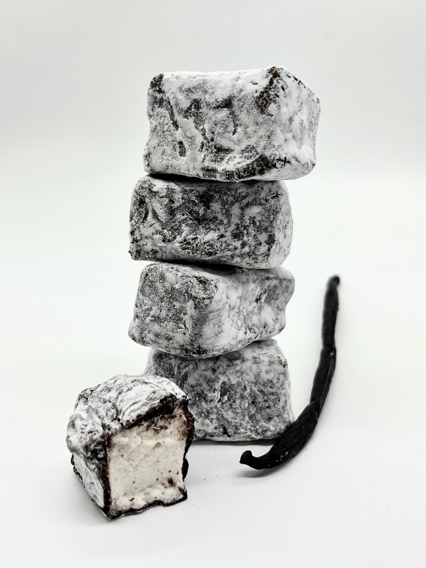 Stack of powdered sugar-covered vanilla ice cream bars with a vanilla bean on a white background