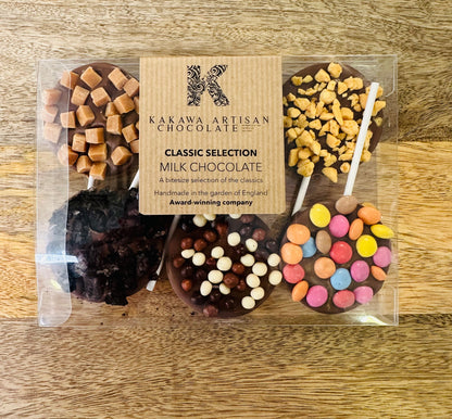Packaged milk chocolate selection with colorful candies on a wooden surface, featuring Kakawa Artisan Chocolates branding.