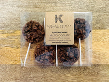 Chocolate fudge brownie lollipops in clear packaging with a Kakawa Artisan Chocolate label on a wooden surface.
