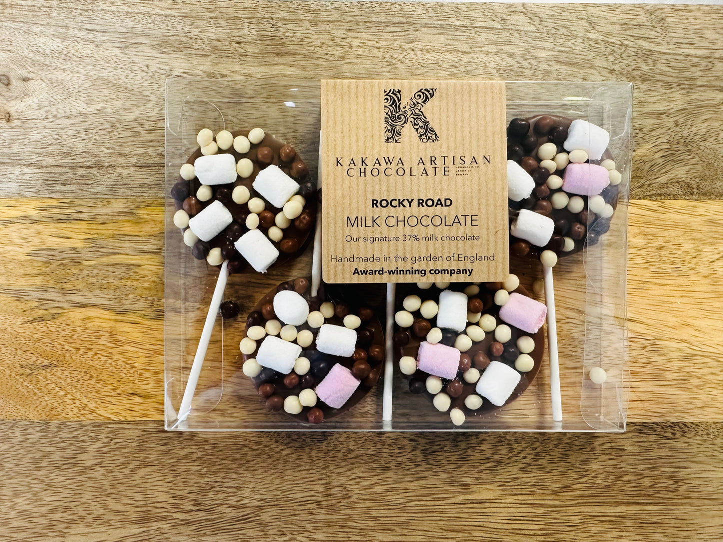 Packaged rocky road chocolate lollipops with a Kakawa Artisan Chocolate label on a wooden surface.