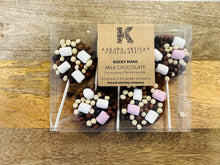 Packaged rocky road chocolate lollipops with a Kakawa Artisan Chocolate label on a wooden surface.