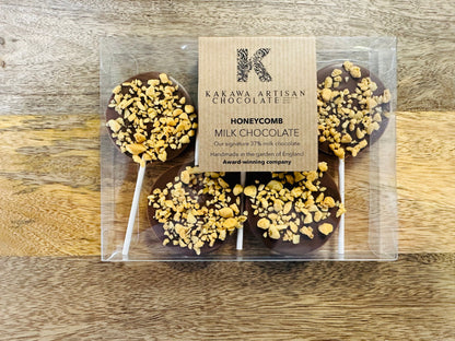 Chocolate lollipops with honeycomb on sticks in a clear packaging against a wooden background