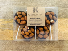 Packaged chocolate lollipops with almonds on a wooden surface, featuring Kakawa Artisan Chocolate branding.