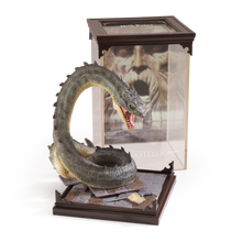 Basilisk figurine on a stand with a book featuring a character's face in the background