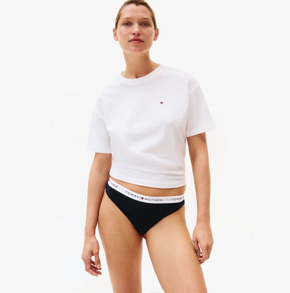 Woman wearing a white t-shirt and black underwear with Tommy Hilfiger logo on a white background