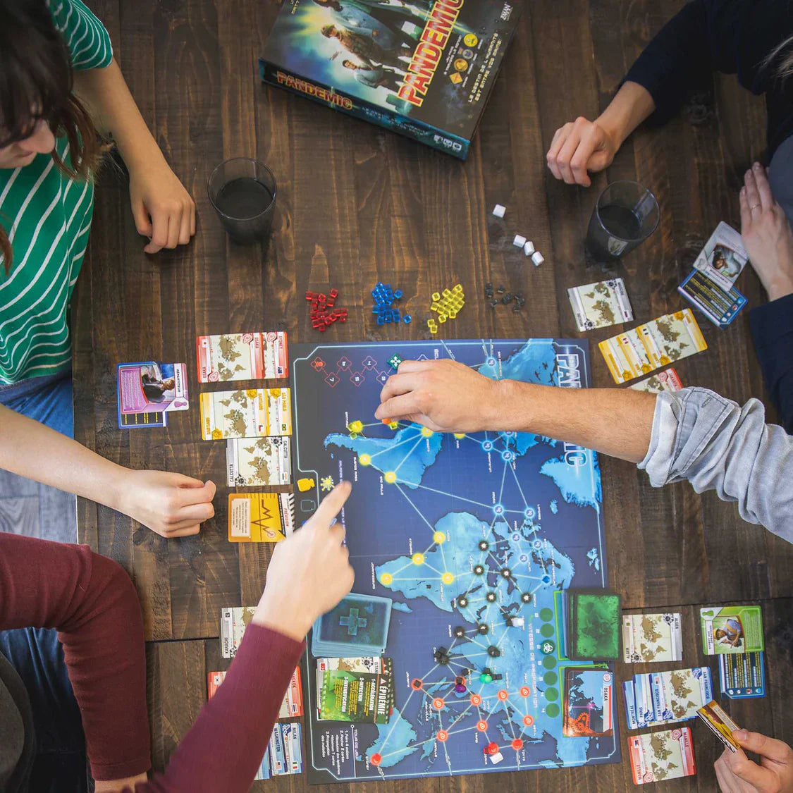 People playing a board game on a wooden table with various game pieces and cards.