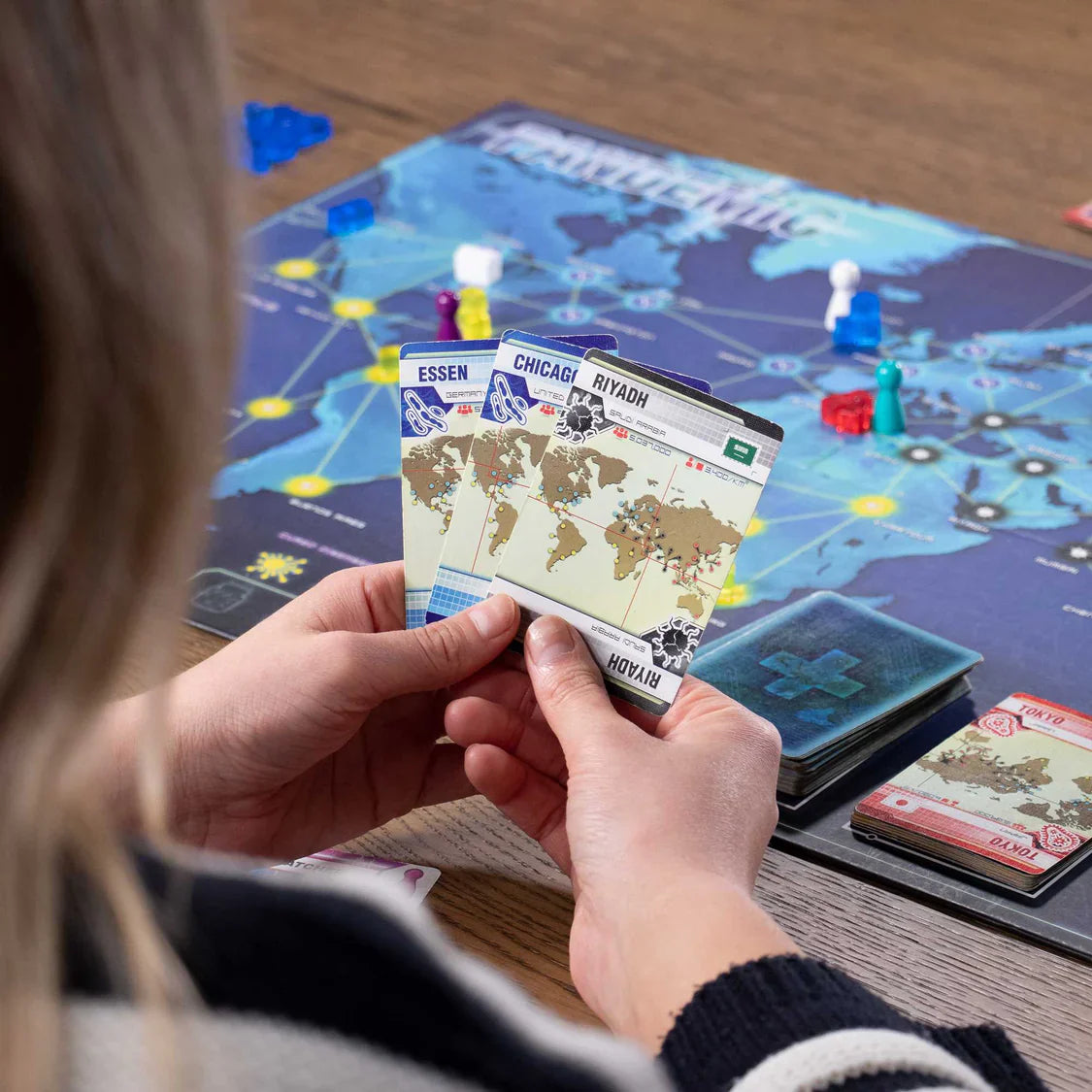 Person holding world map cards over a board game with a map on the table